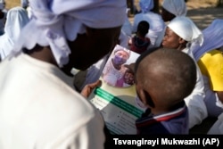 A woman reads a measles vaccination flier with her baby while attending church outside Harare, Friday, Sept. 16, 2022. (AP Photo/Tsvangirayi Mukwazhi)