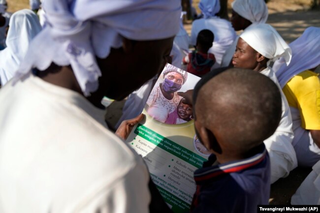 A woman reads a measles vaccination flier with her baby while attending church outside Harare, Friday, Sept. 16, 2022. (AP Photo/Tsvangirayi Mukwazhi)