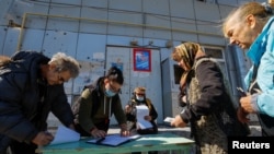 Penduduk setempat antre sebelum menerima surat suara dari anggota komisi pemilihan dan memberikan suara mereka ke dalam kotak suara keliling pada hari ketiga referendum, di Mariupol, Ukraina, 25 September 2022.