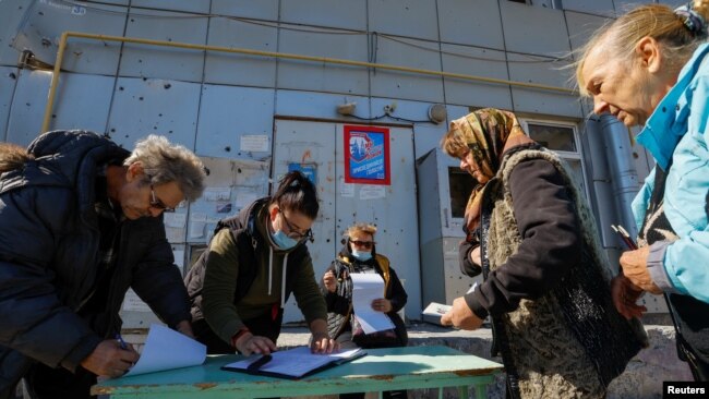 Residentes locales esperan antes de recibir las boletas de los miembros de una comisión electoral y depositar sus votos en una urna móvil en el tercer día de un referéndum, en Mariupol, Ucrania, el 25 de septiembre de 2022.