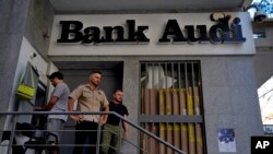 Seorang pria, kiri, menarik uang di ATM, dijaga ketat penjaga keamanan di luar cabang A Bank Audi, di Beirut, Lebanon, Senin, 26 September 2022. (AP/Bilal Husein)