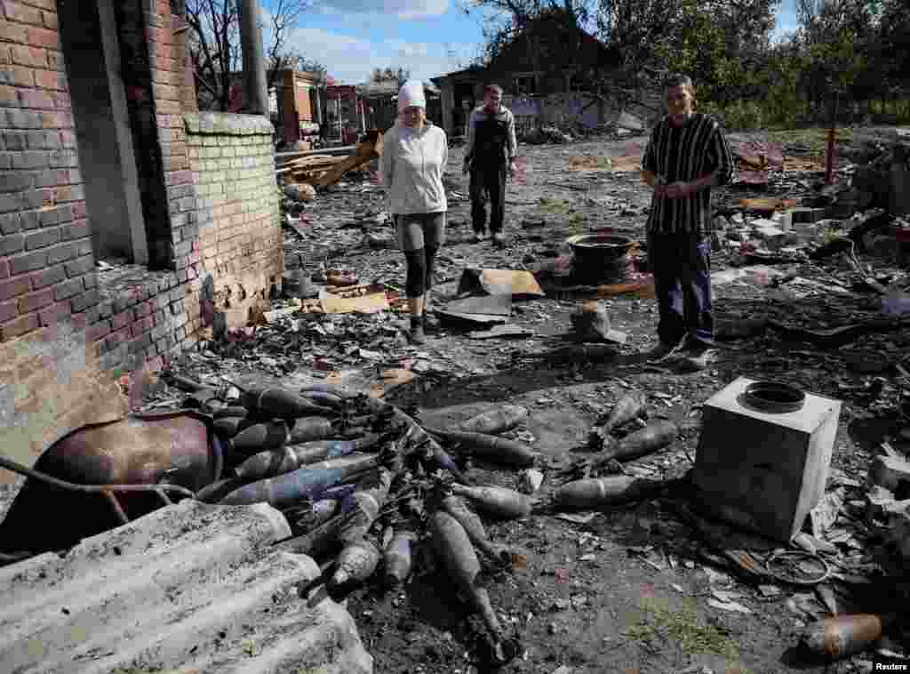 Warga setempat berdiri di dekat amunisi mortir di jalan yang hancur di desa Kamyanka, yang baru-baru ini direbut kembali oleh Angkatan Bersenjata Ukraina, di wilayah Kharkiv, Ukraina (22/9). (Foto: Reuters)&nbsp;