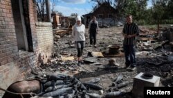 ILustrasi: Penduduk setempat berdiri di dekat amunisi mortir di jalan yang hancur di desa Kamyanka, wilayah Kharkiv, Ukraina yang baru-baru ini dibebaskan oleh Angkatan Bersenjata Ukraina, 22 September 2022. (REUTERS/Gleb Garanich)