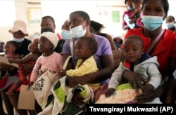 Women holding babies take their places on wooden benches at a clinic in Harare, Zimbabwe, Thursday, Sept. 15, 2022. (AP Photo/Tsvangirayi Mukwazhi)