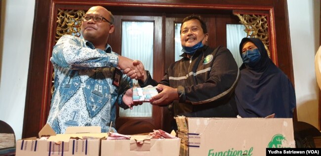 Kepala Kantor Perwakilan BI Solo, Nugroho Joko ( kiri - baju batik) menyerahkan uang baru sebagai pengganti uang tabungan yang dimakan rayap milik Samin (kanan), Kamis (15/9). (Foto: VOA/ Yudha Satriawan)