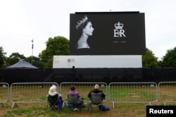 Penggemar kerajaan Isabel Litherland, Martine Knight dan Chris Knight duduk di Hyde Park tempat pemutaran film prosesi pemakaman Ratu Inggris Elizabeth akan berlangsung, di London, Inggris, 14 September 2022. (REUTERS/Andrew Boyers)