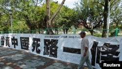资料照：一名男子走过台北街头悬挂的写有“投资中国死路一条”字样的标语。（2012年8月8日）（路透社)