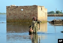 FILE - A man carries some belongings as he wades through floodwaters in Jaffarabad, a flood-hit district of Baluchistan province, Pakistan, Sept. 19, 2022.