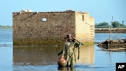 A man carries some belongings as he wades through floodwaters in Jaffarabad, a flood-hit district of Baluchistan province, Pakistan, Sept. 19, 2022. 