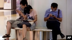 FILE - People sit on a bench inside a shopping mall using their mobile devices, in Beijing, China, Aug. 19, 2013. 