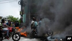 A motorcycle taxi driver carries clients past a burning barricade set by taxi drivers to protest the country's fuel shortage in Port-au-Prince, Haiti, July 13, 2022. 