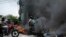 A motorcycle taxi driver carries clients past a burning barricade set by taxi drivers to protest the country's fuel shortage in Port-au-Prince, Haiti, July 13, 2022. 