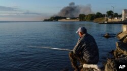 A fisherman watches smoke rise after Russian forces launched a missile attack on a military unit in the Vyshhorod district on the outskirts of Kyiv, Ukraine, July 28, 2022.