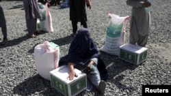 FILE - An Afghan woman waits to receive a food package distributed by a Saudi Arabia humanitarian aid group at a distribution center in Kabul, Afghanistan, April 25, 2022. 