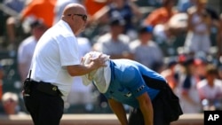 Jefe de preparadores físicos de los Orioles de Baltimore, ayuda al umpire del plato a refrescarse del calor con una toalla húmeda en la cabeza durante un partido entre los Orioles y los Yanquis de Nueva York, el domingo 24 de julio de 2022, en Baltimore. 