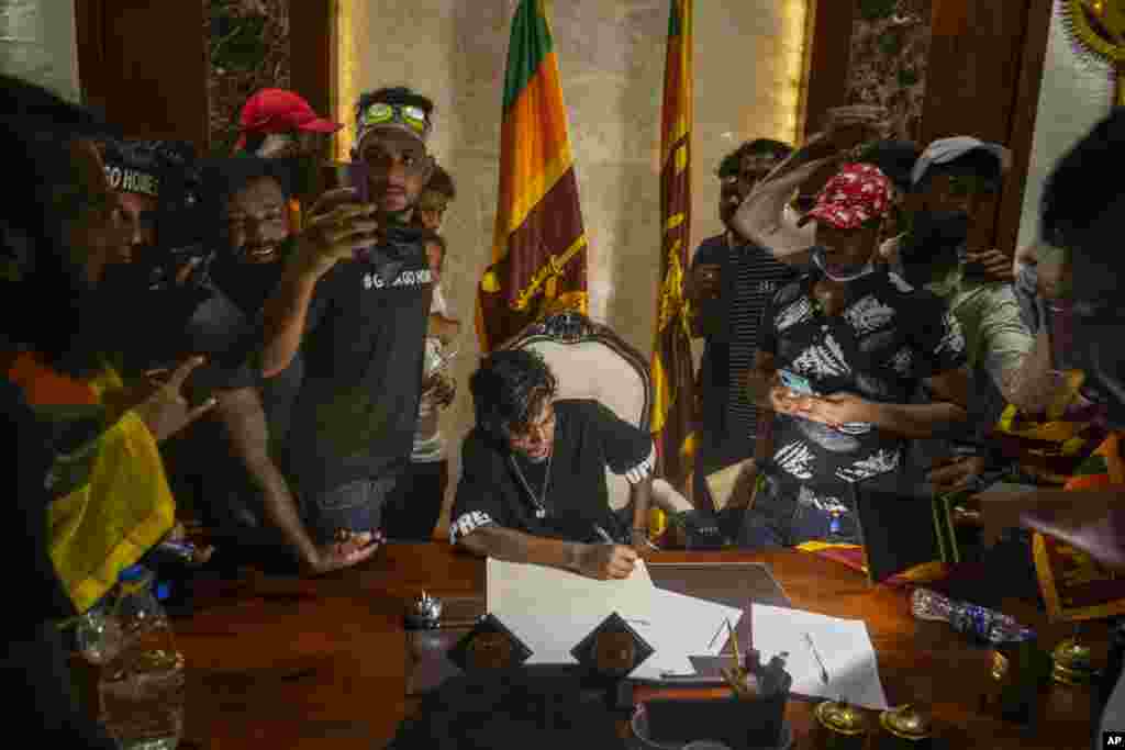A protester sits on a chair surrounded by others after storming Sri Lankan Prime Minister Ranil Wickremesinghe&#39;s office in Colombo, July 13, 2022.