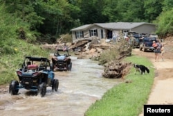 ATV drivers ferrying generator fuel and water drive around a home that was torn from its foundations during flooding and left in the middle of the road, along Bowling Creek, Kentucky, on July 31, 2022. (Chris Kenning/USA Today Network via Reuters)