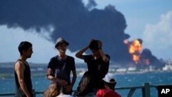 Los jóvenes se reúnen mientras las llamas y el humo siguen saliendo de la Base de Supertanqueros de Matanzas. (Foto AP/Ramón Espinosa)