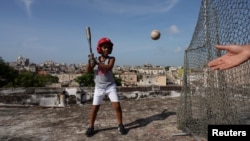 Baseball fan Kevin Kindelan, 8, practices with his father on the roof of their house in Havana, Cuba, June 14, 2022. (REUTERS/Alexandre Meneghini )