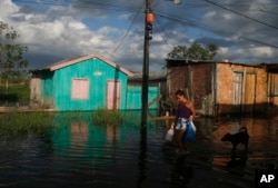 A woman walks on a street flooded by the rise of the Negro river in Iranduba, Amazonas state, Brazil, Monday, May 23, 2022. (AP Photo/Edmar Barros)