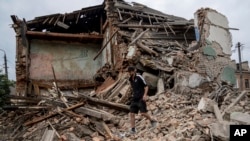 A man searches for documents of their injured friend in the debris of a destroyed apartment house after Russian shelling in a residential area in Chuhuiv, Kharkiv region, Ukraine, Saturday, July 16, 2022.