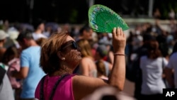 FILE - A tourist uses a fan to shade her face from the sun while waiting to watch the Changing of the Guard ceremony outside Buckingham Palace, during hot weather in London, July 18, 2022.