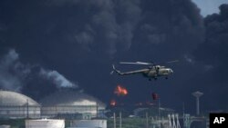 Un helicóptero lleva agua a la base de supertanqueros de Matanzas, mientras los bomberos intentan sofocar el incendio. (Foto AP/Ramón Espinosa)