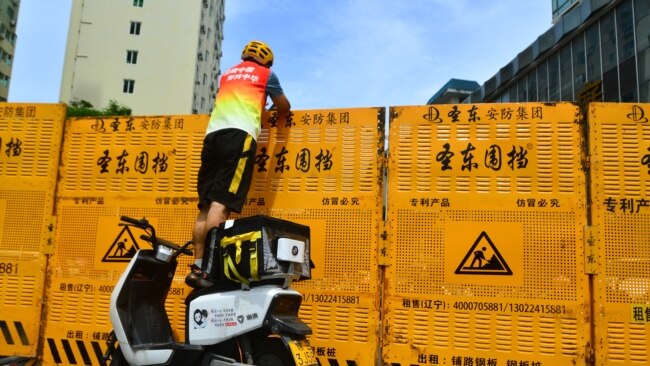 A courier delivers an order over a barricade put up as a measure designed to help curb the spread of COVID-19 in Sanya, Hainan province, China, August 6, 2022. Economists say China's strict zero COVID-19 practices contributed to the country's fiscal slowdown.