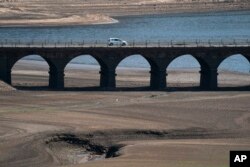 Sebuah mobil melintasi jembatan di Woodhead Resevoir, West Yorkshire, Inggris, Senin, 18 Juli 2022 saat permukaan air turun sangat rendah di tengah suhu panas mencapai rekor di Inggris. (AP/Jon Super)