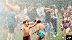 Water rains down on children during the Geneva Water Battle, July 24, 2022, at Memorial Field in Geneva, Ohio. Firetrucks provided relief for hundreds during the event, held on a day when more than 85 million Americans were under excessive heat warnings or advisories.