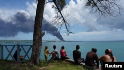 People watch as smoke rises over fuel storage tanks that exploded near Cuba's supertanker port in Matanzas, Cuba, August 7, 2022