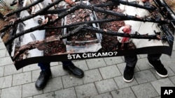 FILE - Members of the Independent Journalists' Association of Serbia hold a poster showing journalist Milan Jovanovic in his burned house that reads: "What are we waiting for?" during a protest in Belgrade, Serbia, Dec. 12, 2019. The protest marked a year since assailants set fire to the house outside Belgrade.