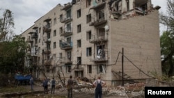 Sejumlah warga lokal mengamati gedung perumahan warga yang hancur akibat serangan pasukan Rusia di Kota Chasiv Yar, wilayah Donetsk, Ukraina, pada 11 Juli 2022. (Foto: Reuters/Gleb Garanich)