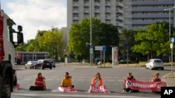 Climate activist Lina Schinkoethe, left, and her mother Solvig Schinkoethe, second from left, sit with their hands glued to the ground during a protest with the group Uprising of the Last Generation in Berlin, Germany, Tuesday, June 21, 2022.