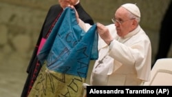 Папа Франциск показує прапор, який йому привезли з міста Буча в Україні, під час його щотижневої загальної аудієнції в залі Павла VI у Ватикані в середу, 6 квітня 2022 р. (AP Photo/Alessandra Tarantino)