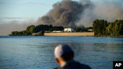 Seorang nelayan mengamati asap yang mengepul di seberangnya setelah pasukan Rusia melancarkan serangan misil ke Distrik Vyshhorod, di pinggiran Kota Kyiv, Ukraina, pada 28 Juli 2022. (Foto: AP/David Goldman)