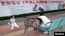 资料照：北京街道上一名小女孩在宣传中国人口与计划生育法的宣传栏下玩耍。 