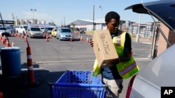 FILE - mA volunteer fills up a vehicle with food boxes at the St. Mary's Food Bank as dozens of vehicles line up in the background, June 29, 2022, in Phoenix.