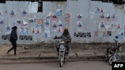 Un chauffeur de moto-taxi attend des clients devant un mur recouvert d'affiches de campagne à Kisumu, dans l'ouest du Kenya, le 16 juillet 2022.
