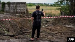 A man takes a photo of a crater of a strike on the second largest Ukrainian city of Kharkiv, Aug. 3, 2022, as the Russia-Ukraine war enters its 160th day.