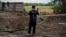 A man takes a photo of a crater of a strike on the second largest Ukrainian city of Kharkiv, Aug. 3, 2022, as the Russia-Ukraine war enters its 160th day.