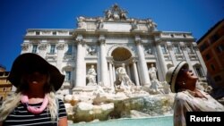 Dua orang perempuan tampak duduk di dekat air mancur Trevi saat cuaca panas saat gelombang panas melanda Eropa di Roma, Italia, 19 Juli 2022. (Foto: Reuters)