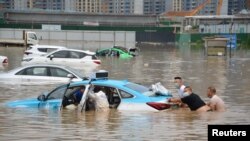 Warga mendorong taksi di stasiun pengisian kendaraan listrik (EV) yang terdampak banjir setelah hujan deras di Lanzhou, provinsi Gansu, Cina 11 Juli 2022. (cnsphoto via REUTERS)