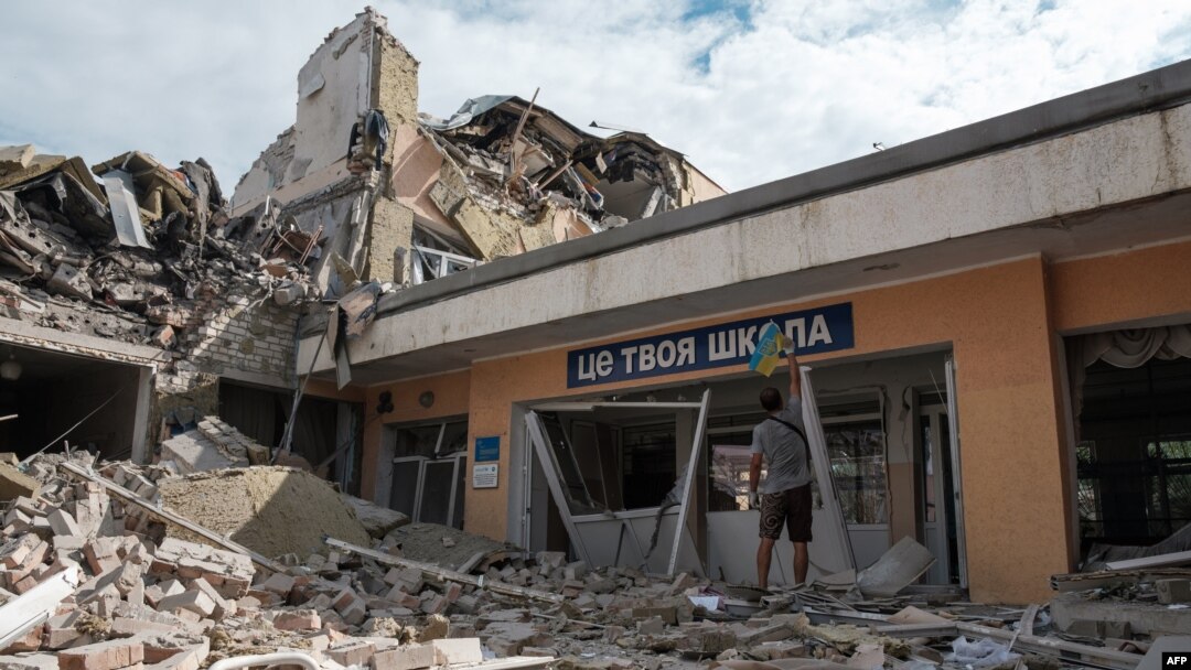 Anton, seorang guru, memasang bendera Ukraina di pintu masuk sekolahnya yang hancur akibat serangan rudal Rusia di kota Bakhmut, wilayah Donetsk Minggu 24 Juli 2022. 