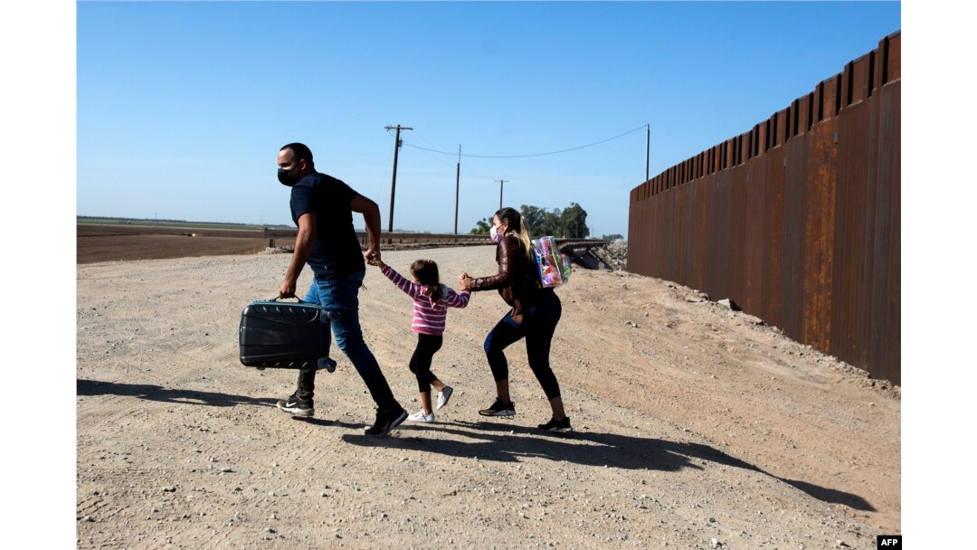 Keluarga migran dari Kuba berlari melintasi perbatasan di dekat tembok yang memisahkan Amerika Serikat dan Meksiko, untuk menyerahkan diri kepada pihak berwenang di Yuma, Arizona, 13 Mei 2021. (RINGO CHIU / AFP)