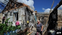 A woman walks near her house while volunteers repair the roof, damaged by shelling in the village of Zalissya, Kyiv region, July 22, 2022, amid the Russian invasion of Ukraine.