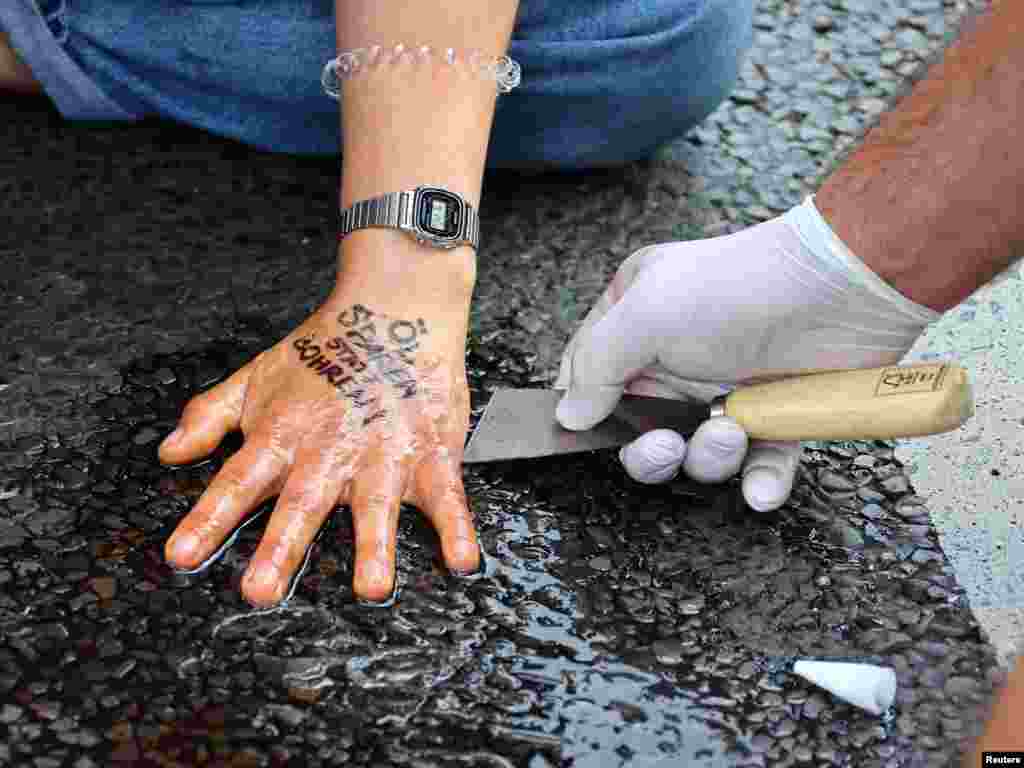 A police officer removes glue from the hand of a Letzte Generation (Last Generation) activist that reads &quot;save oil instead of drill oil,&quot; blocking a road under the slogan &quot;Let&#39;s stop the fossil madness!&quot; for an end to fossil fuels and against oil drilling in the North Sea, in Berlin, Germany.