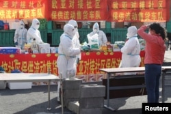 FILE - Workers in protective suits stand by a truck at a mobile grocery store inside a residential compound, following the COVID-19 outbreak in Changchun, Jilin province, China, April 19, 2022. (China Daily via Reuters)