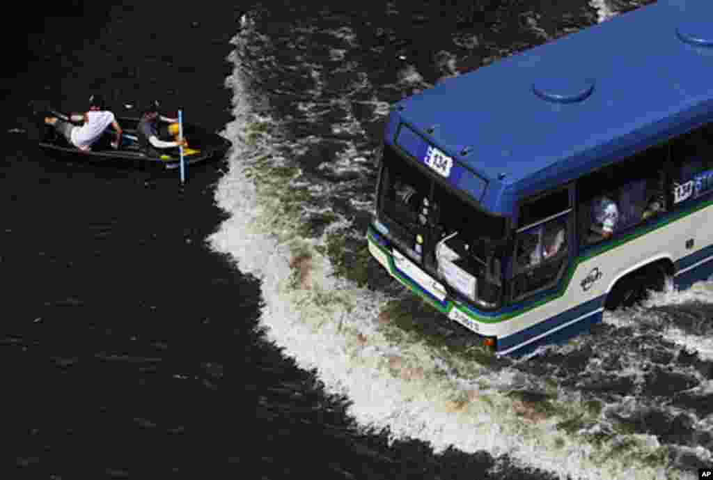 Residents travel on a boat as a bus drives on a flooded street in Bangkok, Thailand, November 5, 2011.