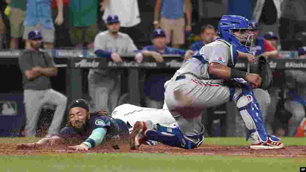 Seattle Mariners&#39; J.P. Crawford slides safely home past Texas Rangers catcher Meibrys Viloria to score the game-tying run on an RBI-double hit by Cal Raleigh during the ninth inning of a baseball game, July 26, 2022, in Seattle, Washington.